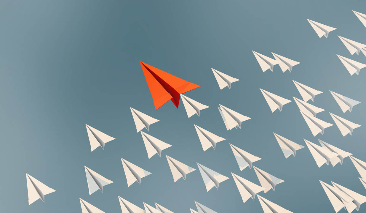 Illustration of paper airplanes flying diagonally as a fleet from bottom right toward upper left. One plane in the lead is colored orange.