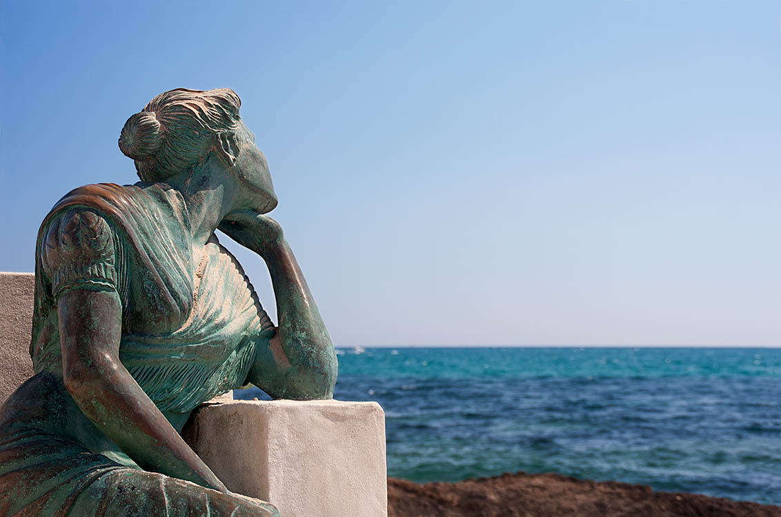 Photo of a sculpture of a woman on a bench looking wistfully out to sea