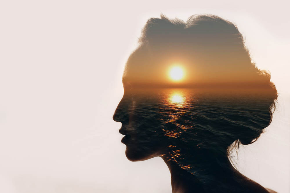 A woman's head is silhouetted with the sunset over the water