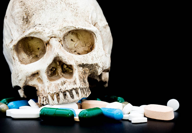 Photo of a human skull sitting on a pile of pills against a black background