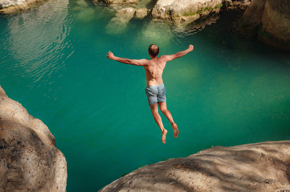 Photo of a man leaping off a rock into green water