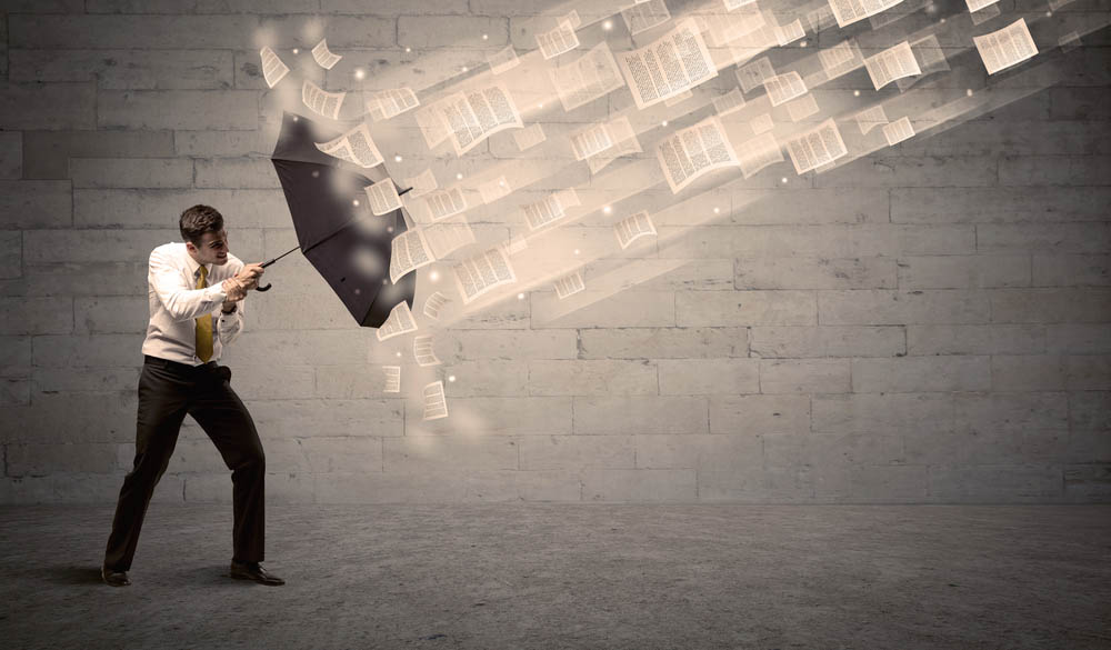 Business man protecting with umbrella against wind of papers concept