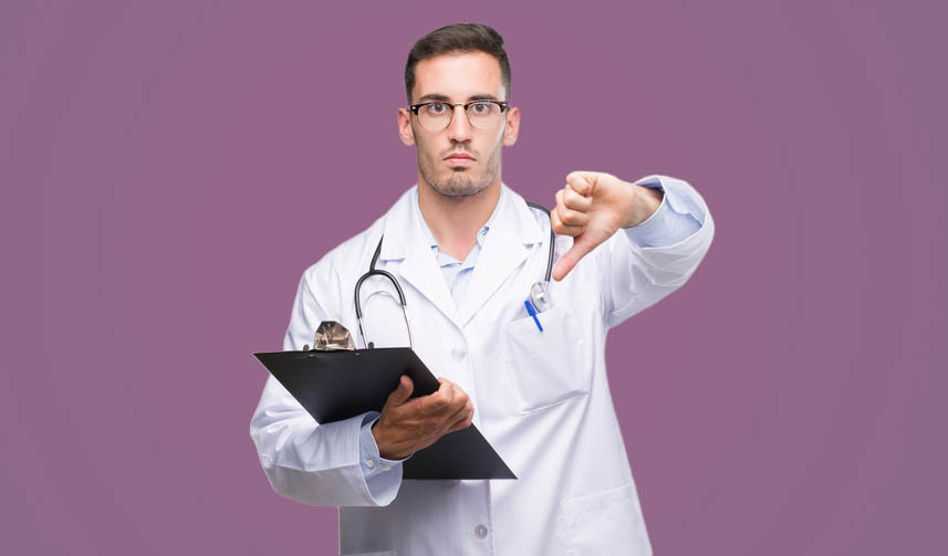 Handsome young doctor man holding a clipboard with angry face, negative sign showing dislike with thumbs down, rejection concept