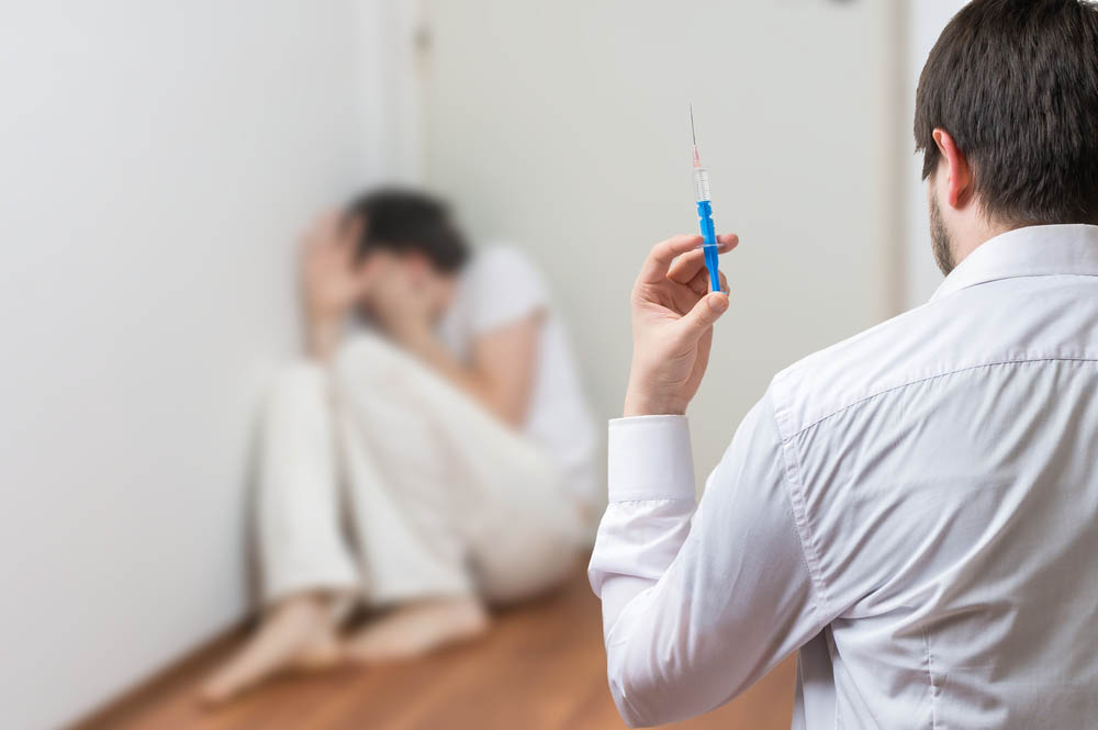 Doctor holding syringe, a patient cringing away in fear out of focus in the background