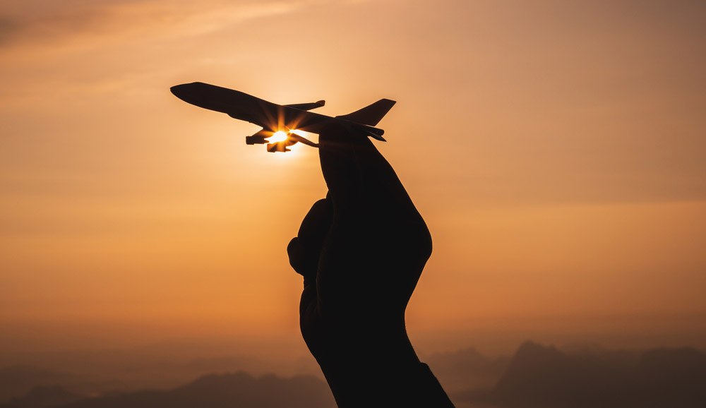 A hand holding a toy plane with sunset light