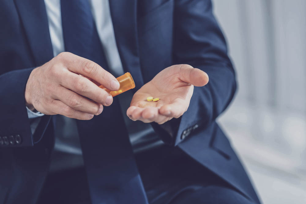 Close up photo depicting a man in a suit pouring two pills into his open palm