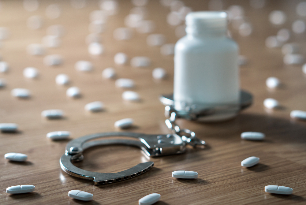 Medicine bottle handcuffed and surrounded by many pills.