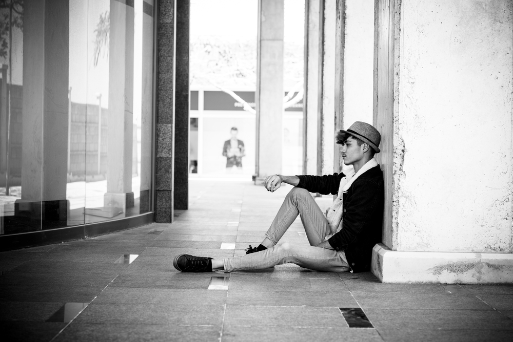 One desperate teenager sitting on the floor in outdoor. Youthful depression young man thoughtful. Lonely boy in poverty. Student people tired and exhausted for school work. Concept of sadness