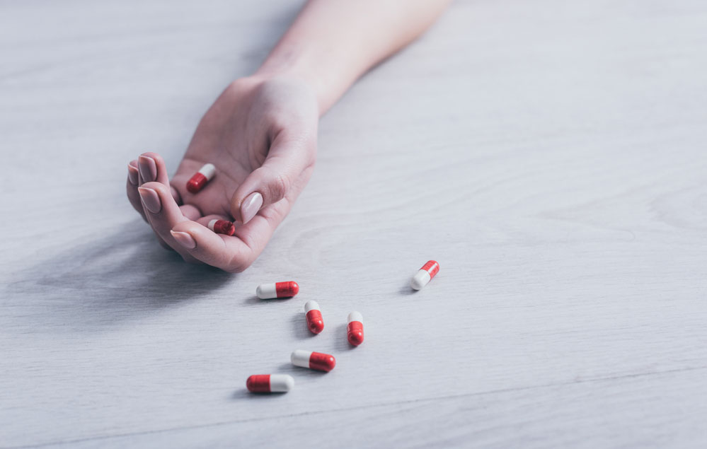 Closeup of a hand lying on the floor with pills spilling out