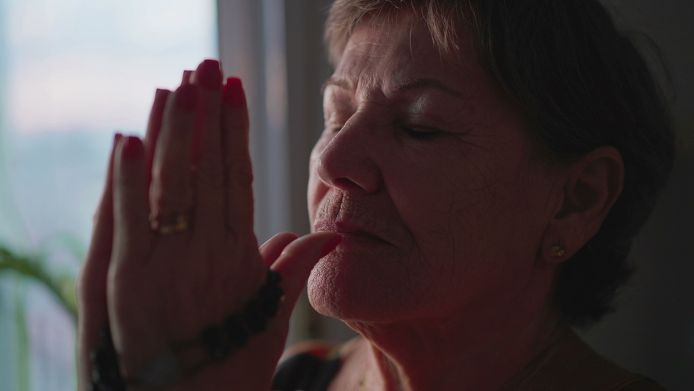 Religious older woman Praying Rosary at home closing eyes in contemplation. 