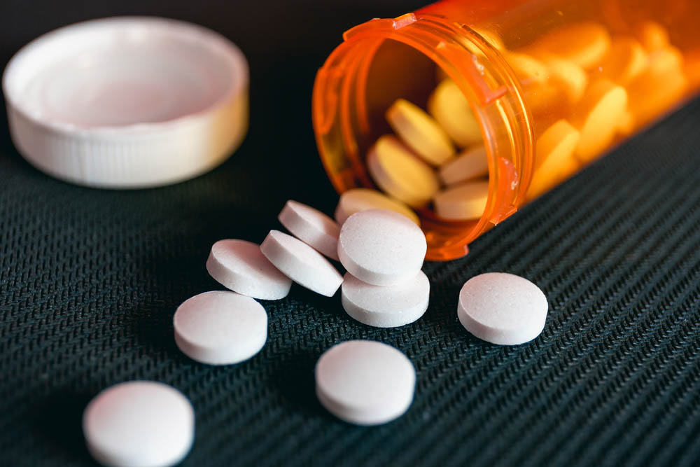 Pills and orange pill bottle on black textured background