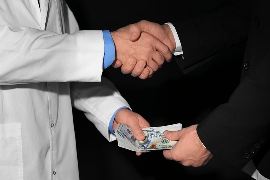 Closeup on hands. White male doctor and businessman shaking hands and passing a bribe with their other hands.