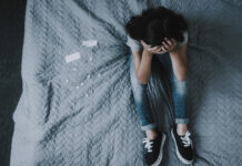 Antidepressants Increase Suicide Attempts in Youth; No Preventative Effect Top View of Girl Sits on Bed with Scattered Pills. Little Child Sitting on Gray Badcover Near Opened Packing of Medicines Keeps Head with Hands. Unhappy Childhood Concept