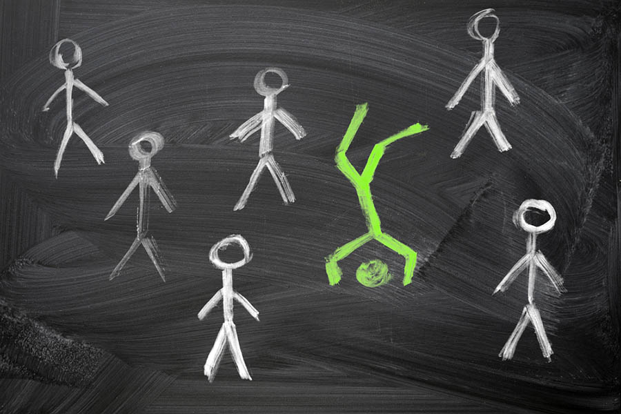 Green stick figure, chalk on a blackboard, standing on its head, amid a crowd of identical white stick figures