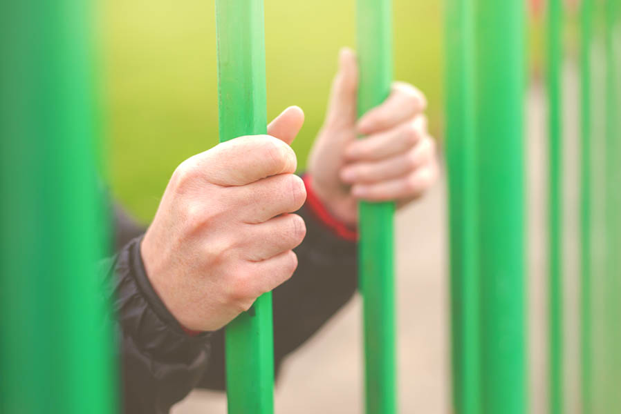 Person behind bars, female hands gripping steel bars, concept of captivity and imprisonment, retro toned, selective focus