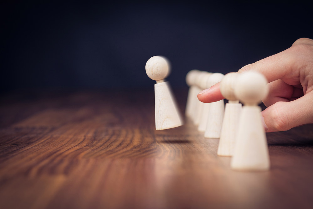 A finger flicks a wooden meeple out of a row of them