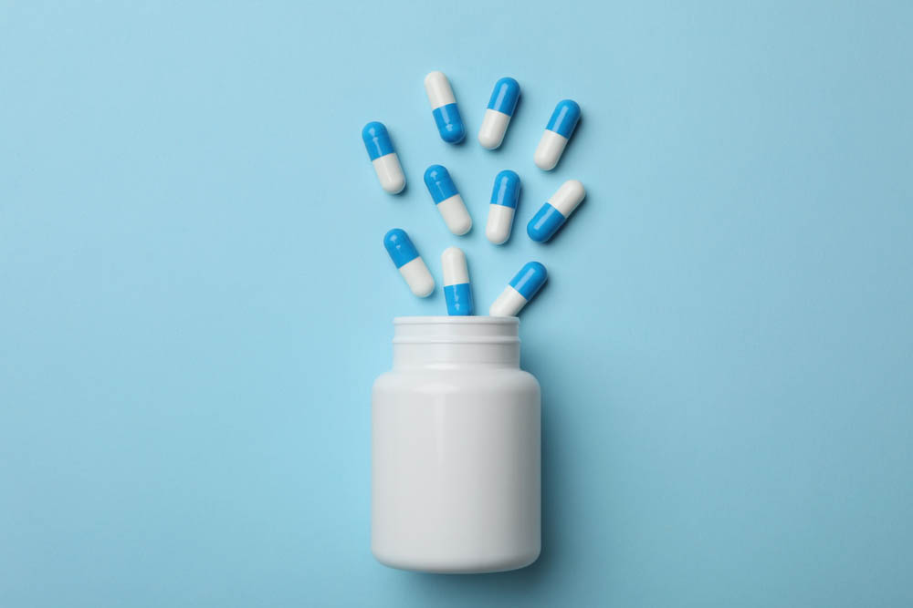 Blue background, white pill bottle, blue and white pills out of the top