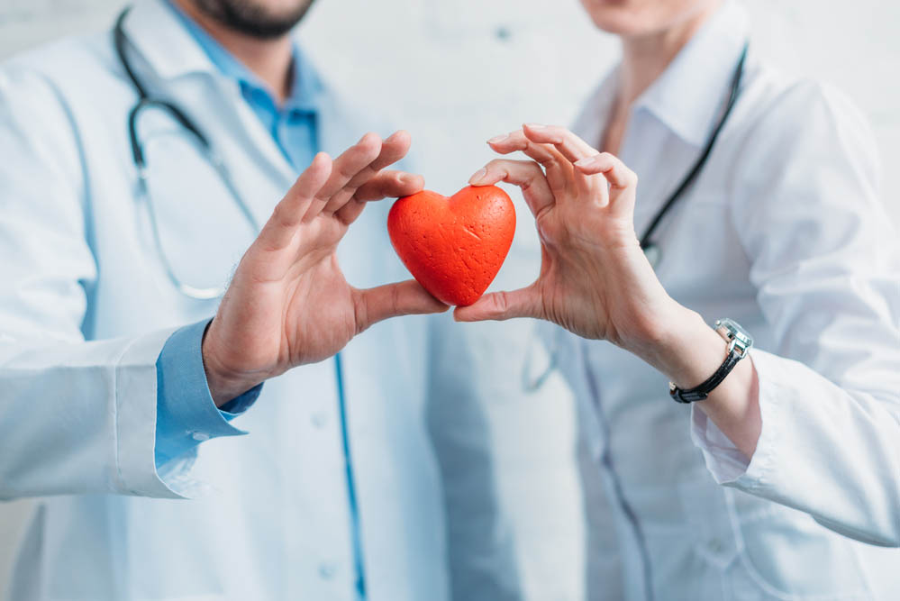 A male and female doctor, out of focus, holding a red toy heart symbol.