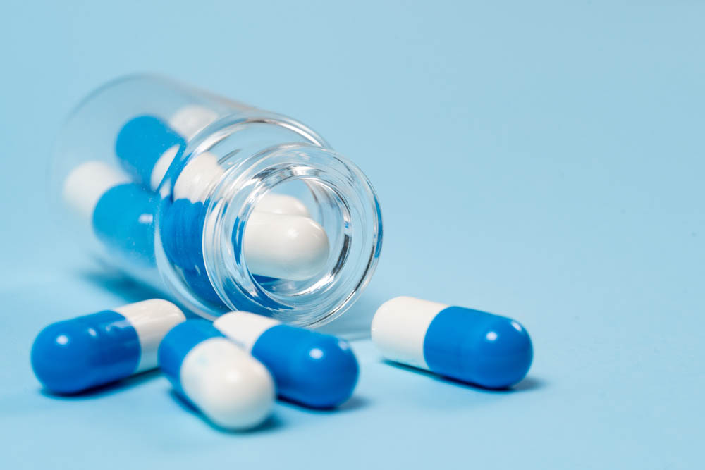 Blue background, transparent pill bottle spills blue and white pills toward camera