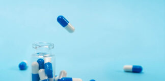 Blue background, transparent pill bottle, blue and white pills out of the top