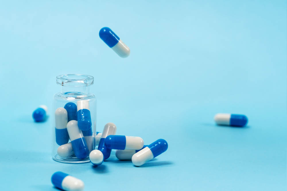 Blue background, transparent pill bottle, blue and white pills out of the top