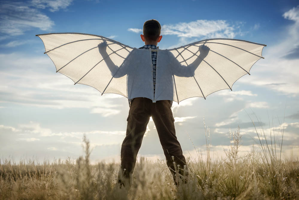 Boy with wings in the field in the afternoon against the blue sky