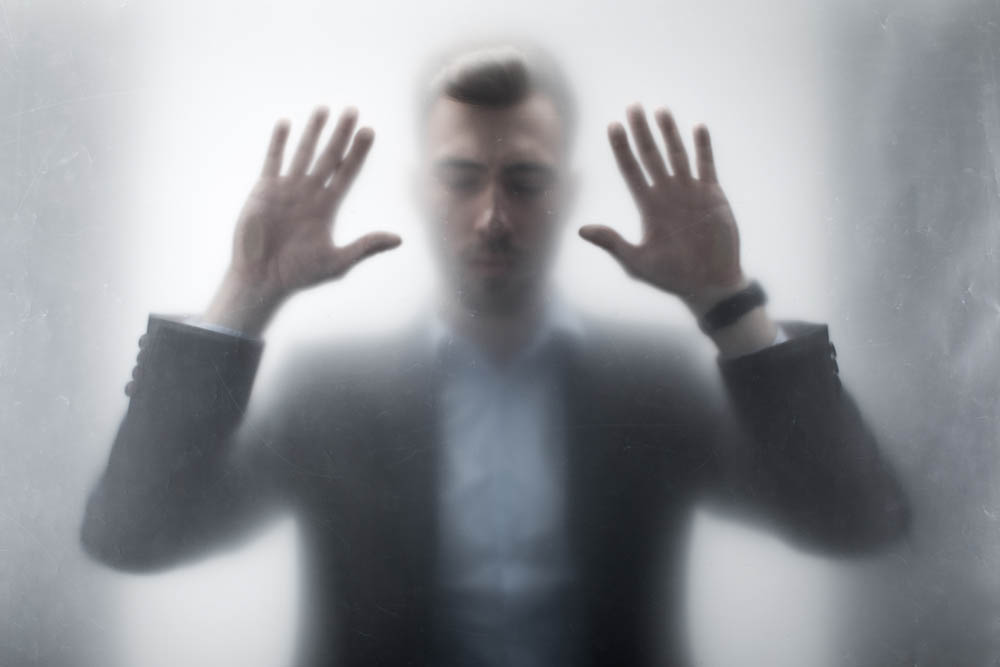 Man with hands against glass, out of focus, looking distressed