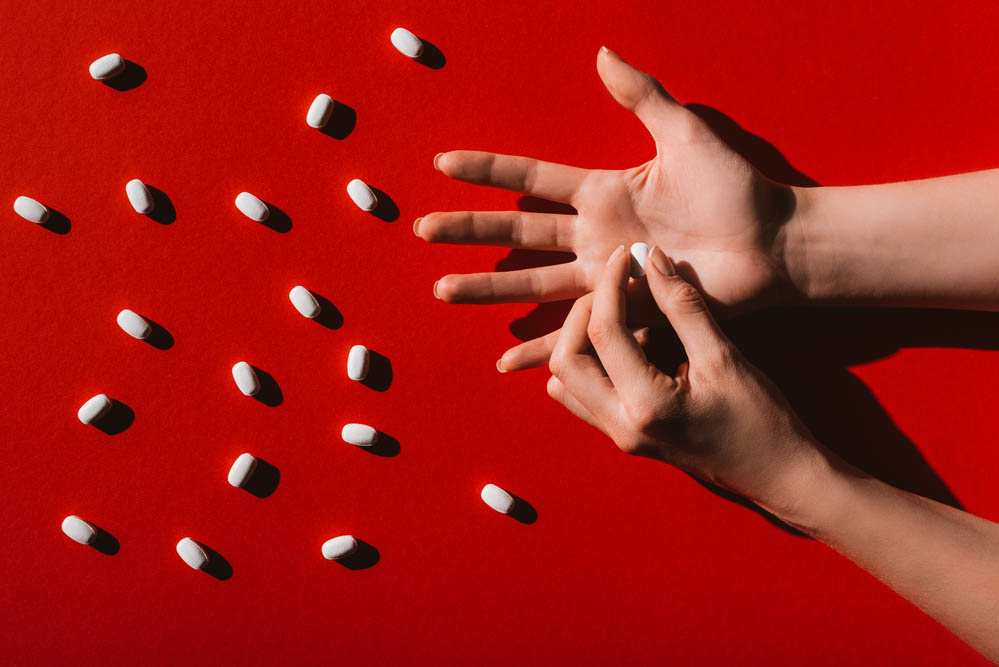 Photo of an open hand on a deep red background with scattered white pills