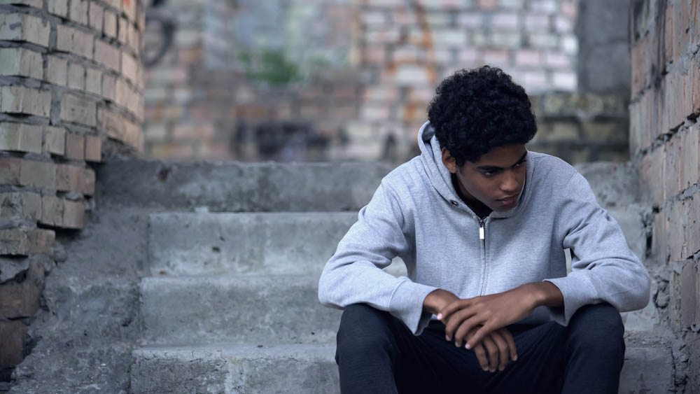 A young man sitting on steps outside looking sad