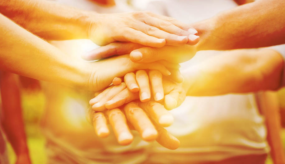 Photo of hands stacking on top of each other in very yellow light