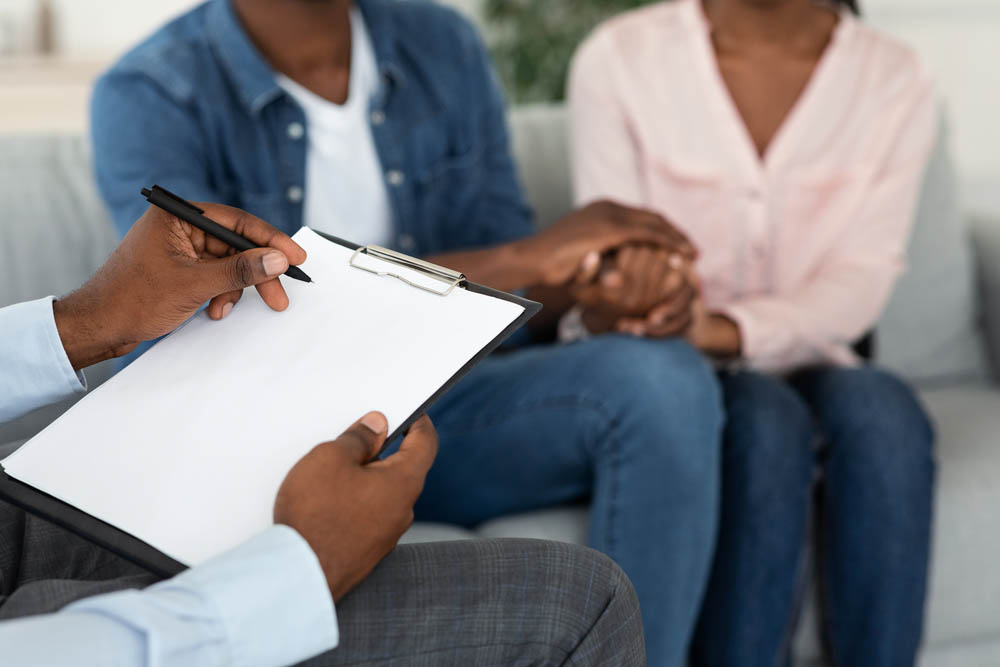 Marital Counselor Taking Notes At Therapy Session With African American Spouses, Holding Blank Clipboard, Filling Information Form At Marriage Counseling Meeting With Blank Couple, Cropped Image