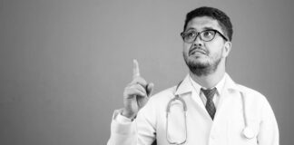 Studio shot of bearded Persian man doctor against gray background in black and white