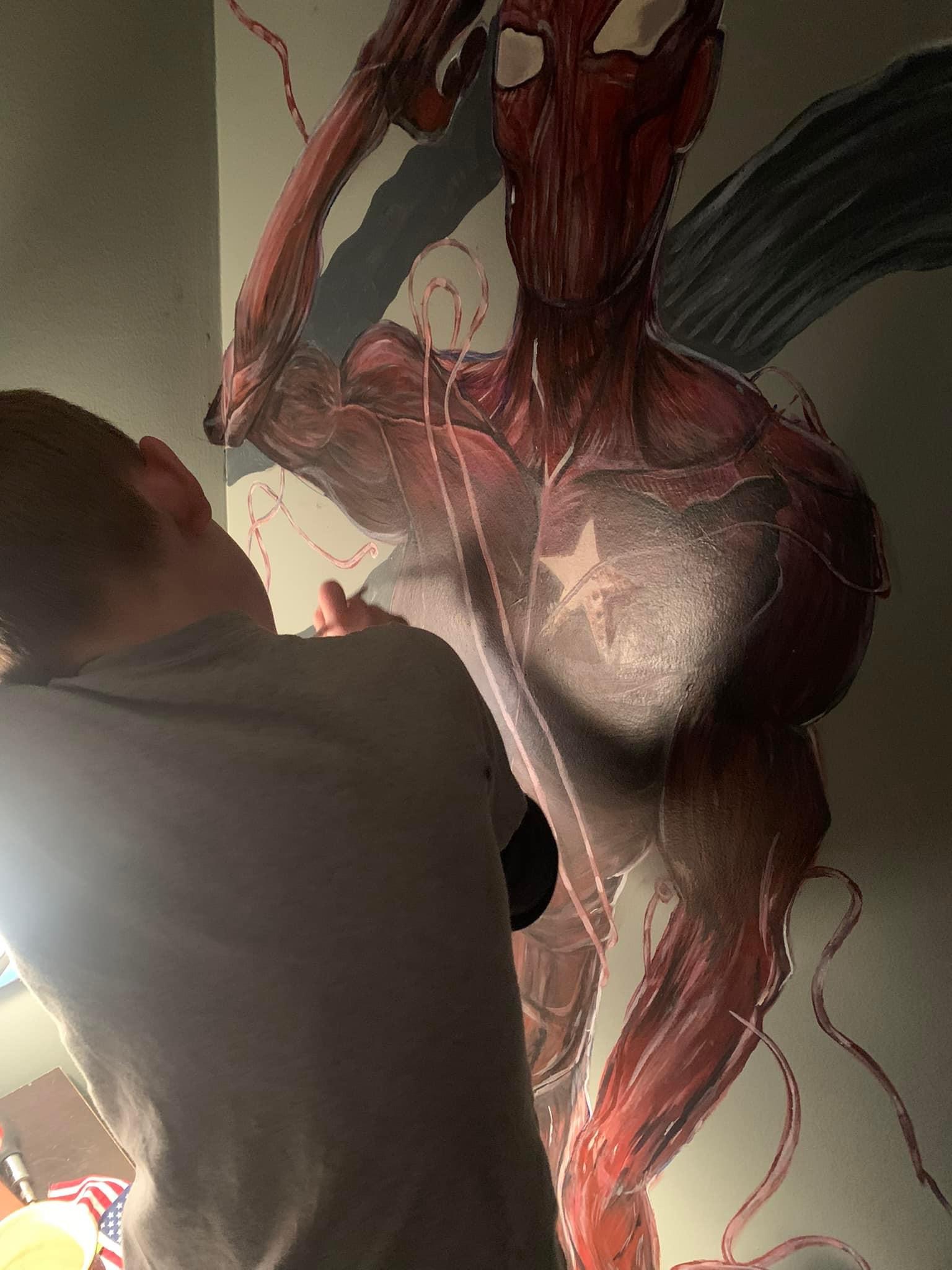 Back of a boy working on a mural of supervillain Carnage