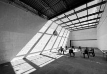 Trust Among Those People in Prison, Rising From the Borderlands Black and white photo of a large room with chairs in a circle, striking light and shadow