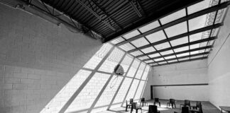 Trust Among Those People in Prison, Rising From the Borderlands Black and white photo of a large room with chairs in a circle, striking light and shadow