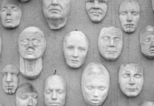 We Are Amidst the Age of Behavioral Alchemy Black and white photo of a wall with faces on it like masks
