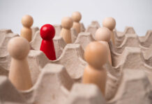 The Core Error of Psychiatrists and Psychologists: Certainty about “Consensus Reality” Macro photography of wooden blocks representing people. One red one stands among wood-colored ones.