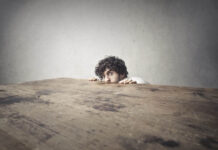 The Trauma Craze: How the Expansion of Trauma Diagnoses Fueled Victimhood Culture A man hiding behind a large wooden table, only his head and hands showing