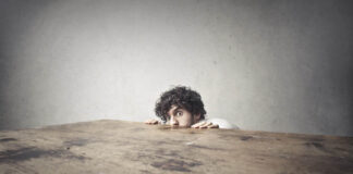 The Trauma Craze: How the Expansion of Trauma Diagnoses Fueled Victimhood Culture A man hiding behind a large wooden table, only his head and hands showing