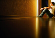 The Fallacy of Modern Psychiatry: Treating Symptoms, Ignoring Causes Person sitting in the distance, yellow light corridor