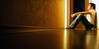 The Fallacy of Modern Psychiatry: Treating Symptoms, Ignoring Causes Person sitting in the distance, yellow light corridor