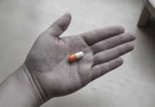 Black and white photo of a hand holding a colorized pill