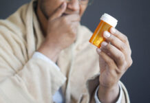 A person, out of focus, holding a pill bottle in focus