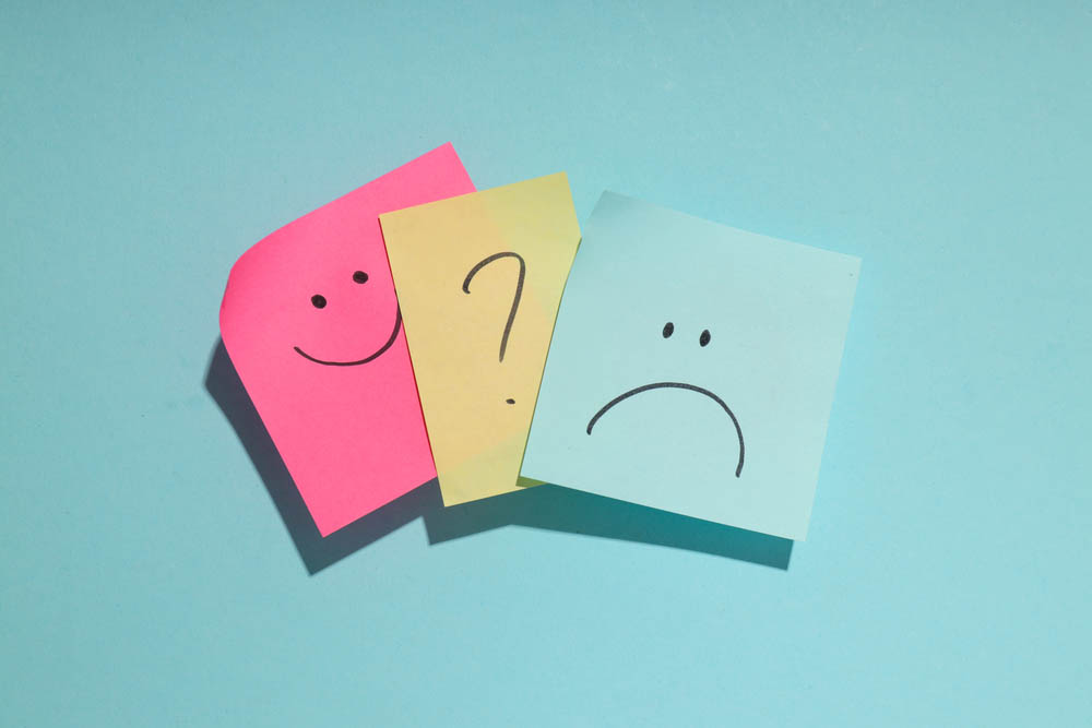 Sticky notes on blue background. One shows a smiley face, one a frown, and one between them depicts a question mark.