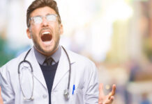 A male doctor appears to scream in frustration. His glasses catch the light