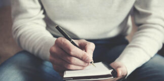 The Wound That Speaks A man is sitting on a sofa and writing notes in a notebook