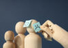 A wooden hand touches post it notes of smiling and sad faces on wooden figures