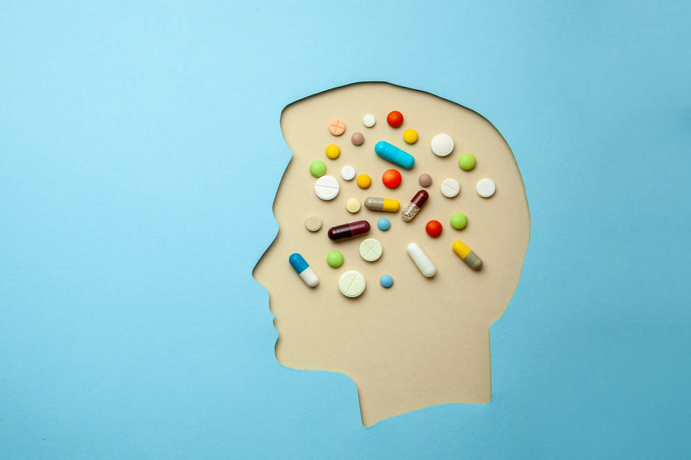 A cutout of a head as if made of blue paper. The head is full of pills.