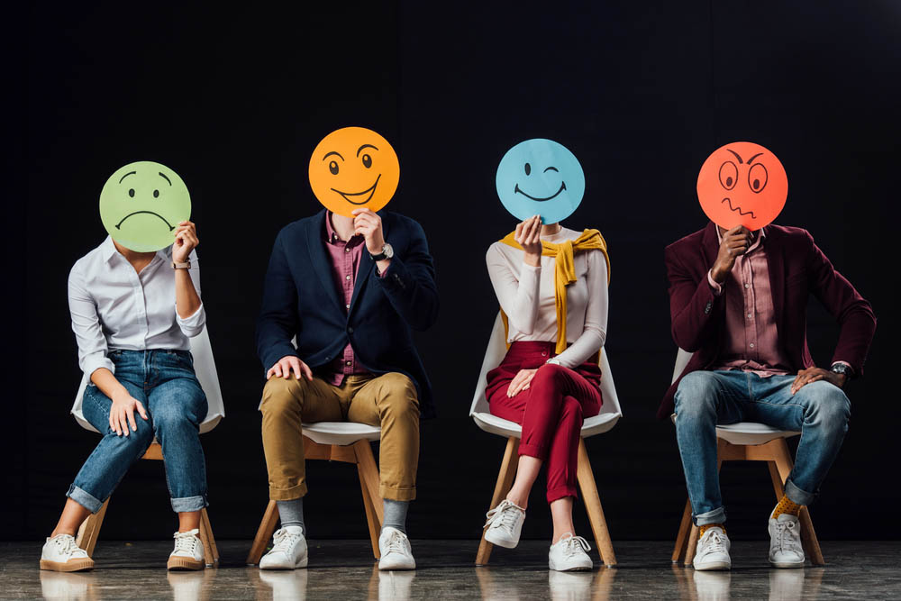 Photo of people holding round hand-drawn faces over their own faces, each depicting an emotion