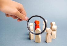 Magnifying glass is looking at the People stand in a circle on a gray background. Communication. Business team, teamwork, team spirit. Wooden figures of people. A circle of people. Selective focus